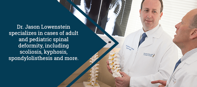 dr jason lowenstein holding spine model in front of spine x-ray